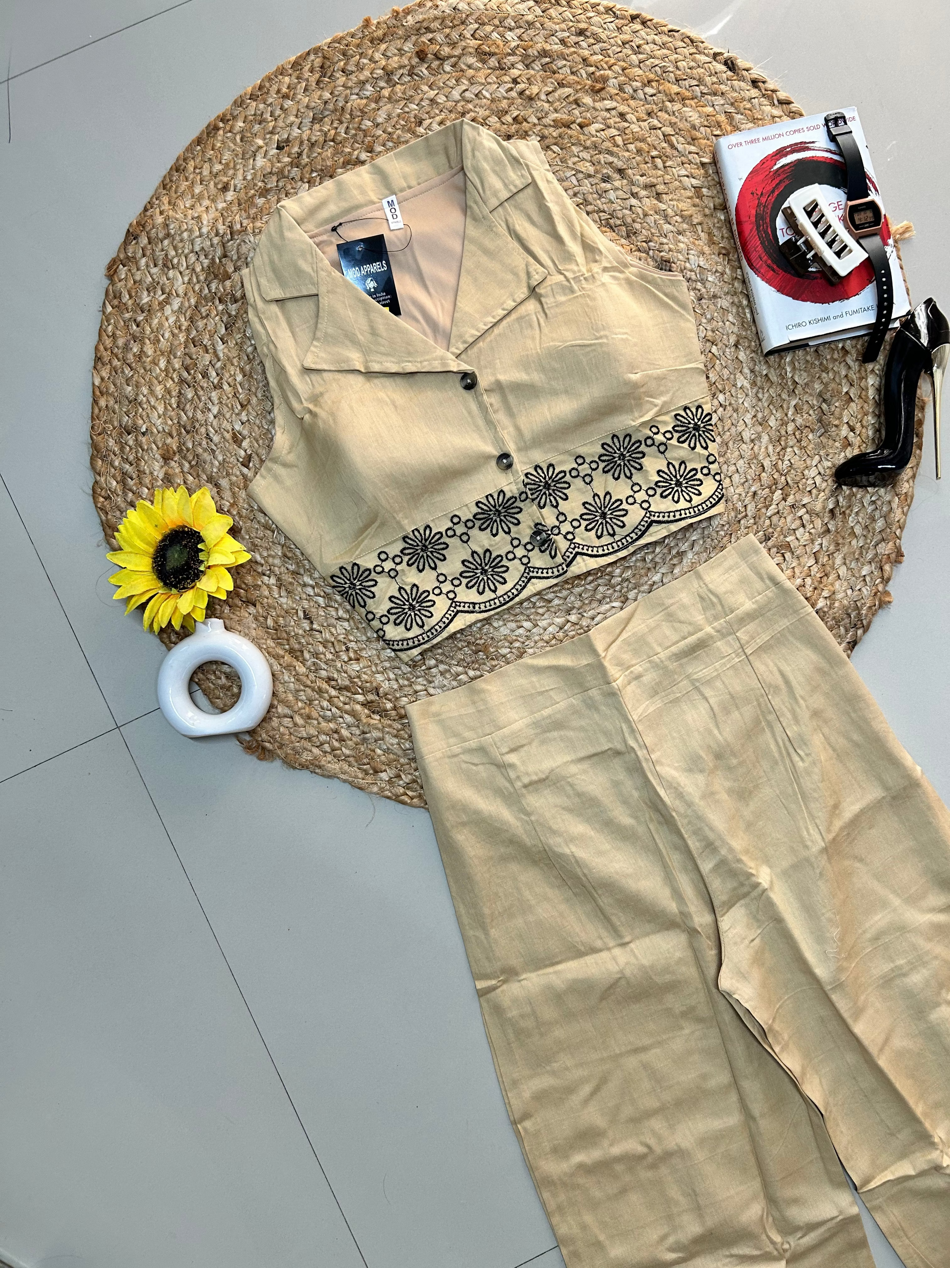 Beige garment with black embroidery on a woven mat with a sunflower and roll of tape.